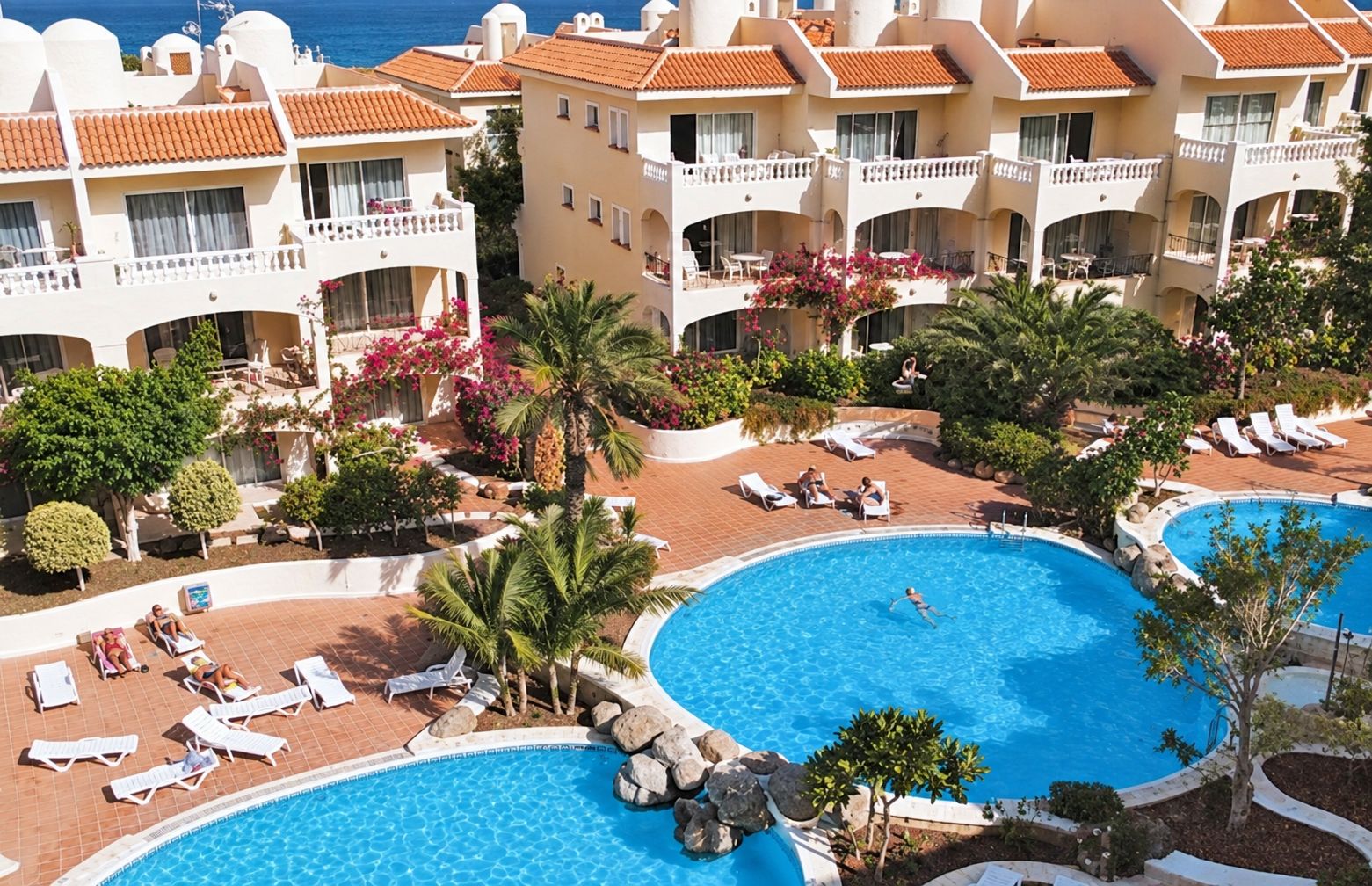 Ein Resort mit mehreren Schwimmbecken, Liegestühlen und Meerblick.