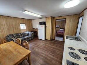 A compact kitchen with a refrigerator, stove, and microwave. There is a wooden dining table and a striped sofa. A small table and chairs are also visible.