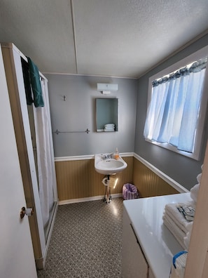 A bathroom with a sink, mirror, towel rack, and window with curtains.