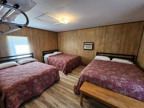 A room with two beds, wooden walls, a ceiling fan, and an air conditioning unit.