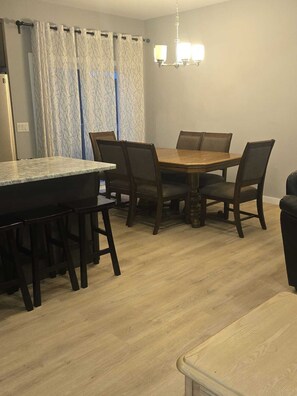 A dining area with a wooden table and chairs, a chandelier, and a window with curtains.