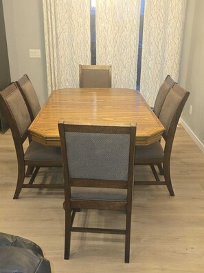 A dining table with four chairs, a window with curtains, and a light switch on the wall.