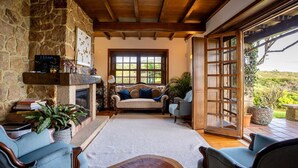 A cozy living room with a stone fireplace, a sofa, and a view through a large window. - Villa Atlantico, nestled where Sintra Mountains meet Atlantic ocean (Colares)
