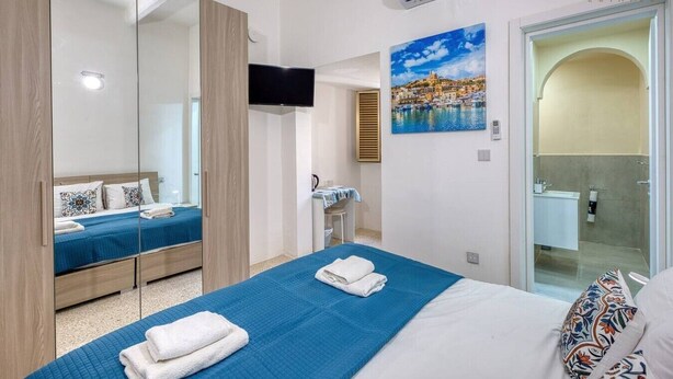 Une chambre d’hôtel avec un lit, une télévision, un tableau et une salle de bain visible à travers une porte ouverte.