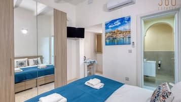 A hotel room with a bed, a TV, a painting, and a bathroom visible through an open door.