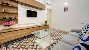 Un salon moderne avec un canapé, une table basse en verre, un téléviseur fixé au mur et un sol à motifs.