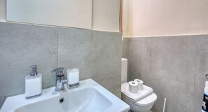 Et badeværelse med vask, to sæbedispensere, toilet og toiletpapir.