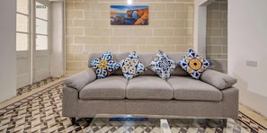 Ein graues Sofa mit gemusterten Kissen, ein Fliesenboden, ein an der Wand befestigtes Bild und eine Tür mit einem Ausgangsschild.