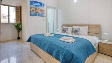 A bedroom with a bed, a nightstand, a potted plant, a painting, and a door.