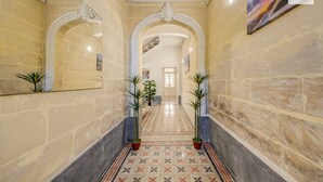 Un couloir aux murs en pierre, au sol carrelé, et agrémenté de deux plantes en pot.