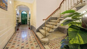 Un couloir avec des carreaux de sol à motifs, une porte verte et un escalier doté d’une rampe en fer forgé.