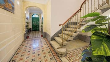 A hallway with patterned floor tiles, a green door, and a staircase with a wrought iron railing.