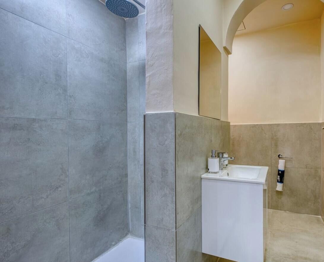 Ein modernes Badezimmer mit grauen Fliesen, einem weißen Waschbecken und einem großen Spiegel.
