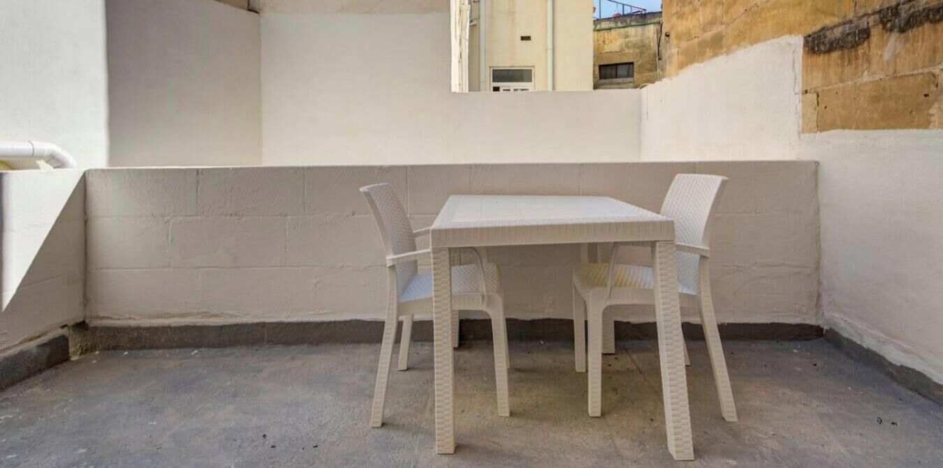 A small outdoor patio area with a white table and two wicker chairs.