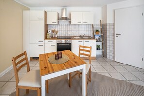 Una cucina compatta con mobili bianchi, un tavolo da pranzo in legno e un forno integrato.