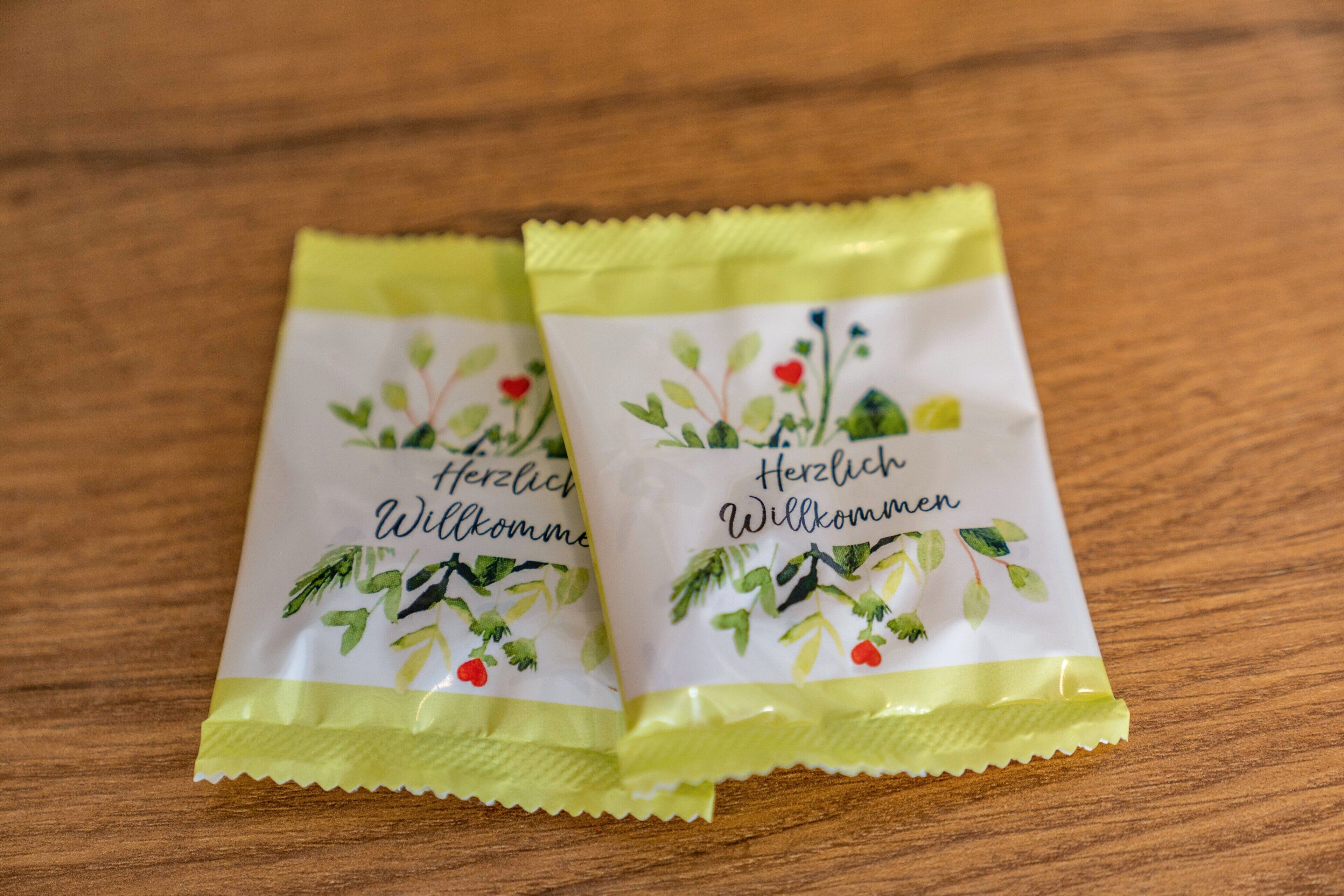 Två paket med texten ”Herzlich Willkommen” och blommönster, placerade på en träyta.