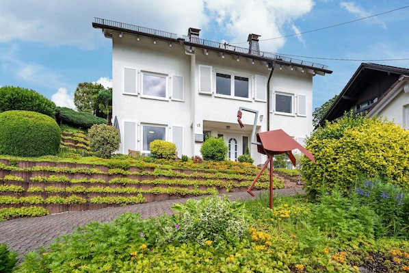 A two-story house with a sloped roof, white exterior, and a balcony on the upper floor.