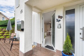 Ein Hauseingang mit Tür, Briefkasten, Blumentopf und Gartenmöbeln.
