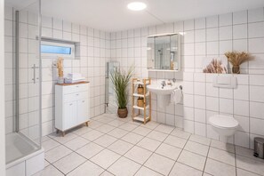 Un bagno moderno rivestito di piastrelle bianche, con box doccia in vetro, lavandino bianco e servizi igienici.