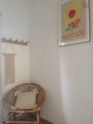 Ein Korbstuhl mit Kissen, ein Wandbehang aus Makramee und ein gerahmtes Kunstwerk mit dem Text 'HOSSEGOR'.