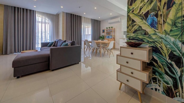 Un soggiorno moderno con un divano, un'area pranzo con sedie, un mobile in legno e un grande quadro a tema tropicale.