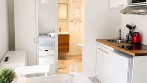A modern hotel room with a dining area, kitchenette, and a bathroom visible through an open door.