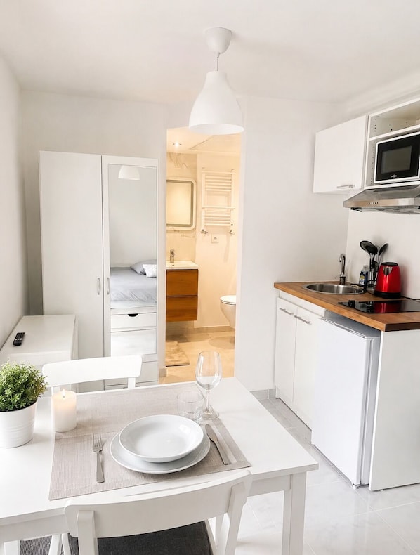 A modern hotel room with a dining area, kitchenette, and a bathroom visible through an open door.
