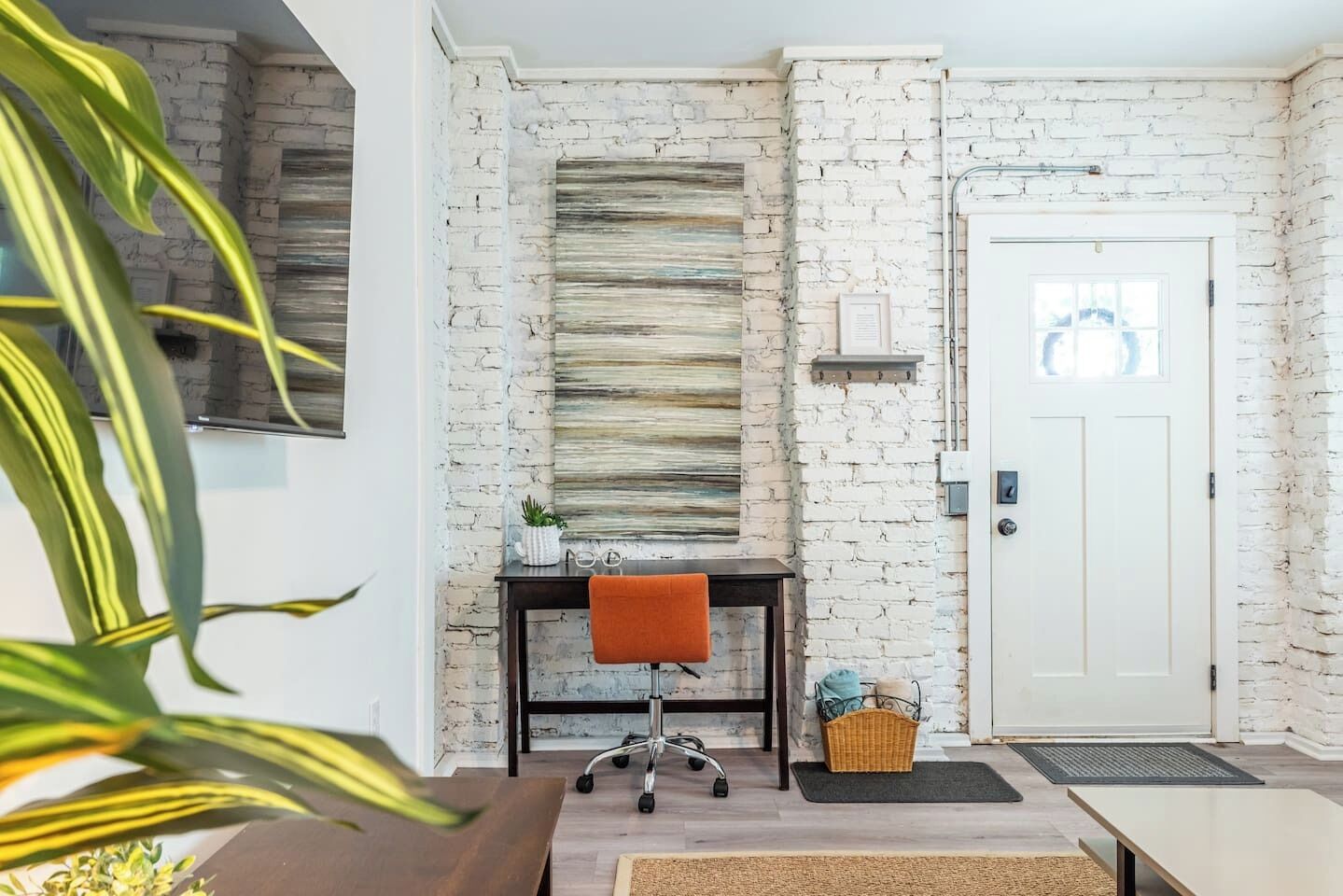 Une pièce avec une porte blanche, un bureau avec une chaise, une plante et un mur à motifs.