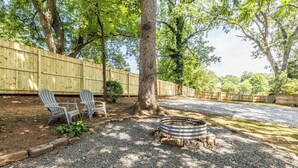 Ein Garten mit Kiesweg, zwei Adirondack-Stühlen, einer Feuerstelle und einem Holzzaun.