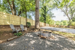 Ein Garten mit Kiesweg, zwei Adirondack-Stühlen, einer Feuerstelle und einem Holzzaun.