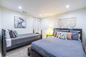 Une chambre avec deux lits, une table de chevet, une lampe et une décoration murale en macramé.