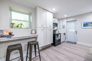 A modern kitchen with white cabinets, a black stove, and a window with plants. - 2 Blocks to Grant Park & Zoo | Firepit + Courtyard (Atlanta)