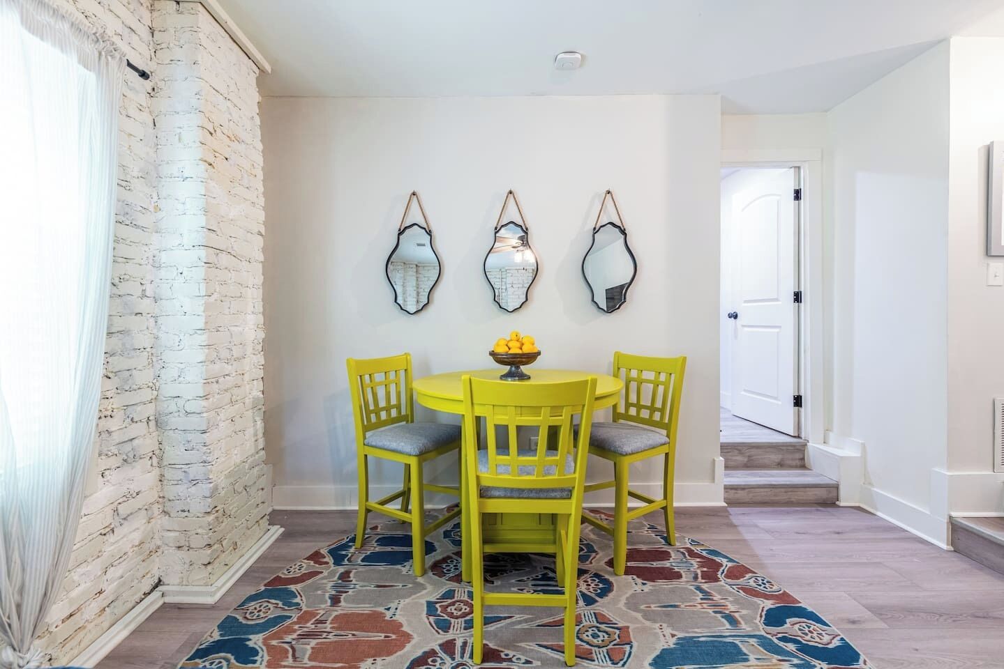 A dining area with a round yellow table, two yellow chairs, and a patterned rug.