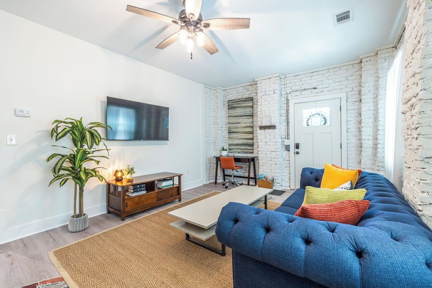 A living room with a blue sofa, a wooden coffee table, a TV mounted on the wall, and a ceiling fan.