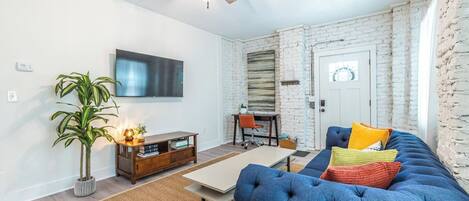 A living room with a blue sofa, a wooden coffee table, a TV mounted on the wall, and a ceiling fan.