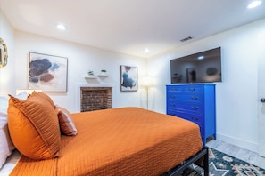 Ein Schlafzimmer mit einem Bett, einer blauen Kommode, einem Kamin und Bildern an den Wänden.