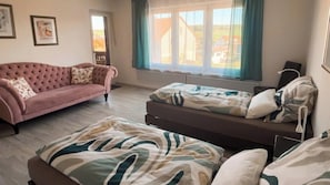 A bedroom with a pink sofa, a bed with patterned bedding, and a window with curtains. - 85 sqm apartment near Würzburg: 3 bedrooms. For families & business travelers (Uettingen)