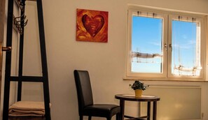 A room with a black chair, a small table with a plant, a window with curtains, and a painting of a heart on the wall. - 85 sqm apartment near Würzburg: 3 bedrooms. For families & business travelers (Uettingen)
