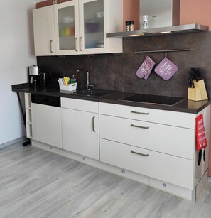 A modern kitchen with a black countertop, white cabinets, a stainless steel range hood, and a hanging rack with two purple towels. - 85 sqm apartment near Würzburg: 3 bedrooms. For families & business travelers (Uettingen)