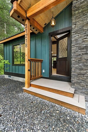 A wooden porch with a stone wall, a number '31218' on the post, and a door with a lattice design. - 2-bedroom house in adorable Ashford with, AC, EV Charger, Hot Tub Wifi (Ashford)