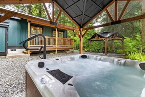 A hot tub in a wooden deck area with a gazebo and a building in the background. - 2-bedroom house in adorable Ashford with, AC, EV Charger, Hot Tub Wifi (Ashford)