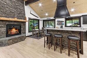A modern kitchen with a stone fireplace, wooden ceiling, and large windows. - 2-bedroom house in adorable Ashford with, AC, EV Charger, Hot Tub Wifi (Ashford)