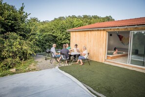 Un groupe de personnes est assis à une table à l’extérieur, avec un bâtiment en bois en arrière-plan.