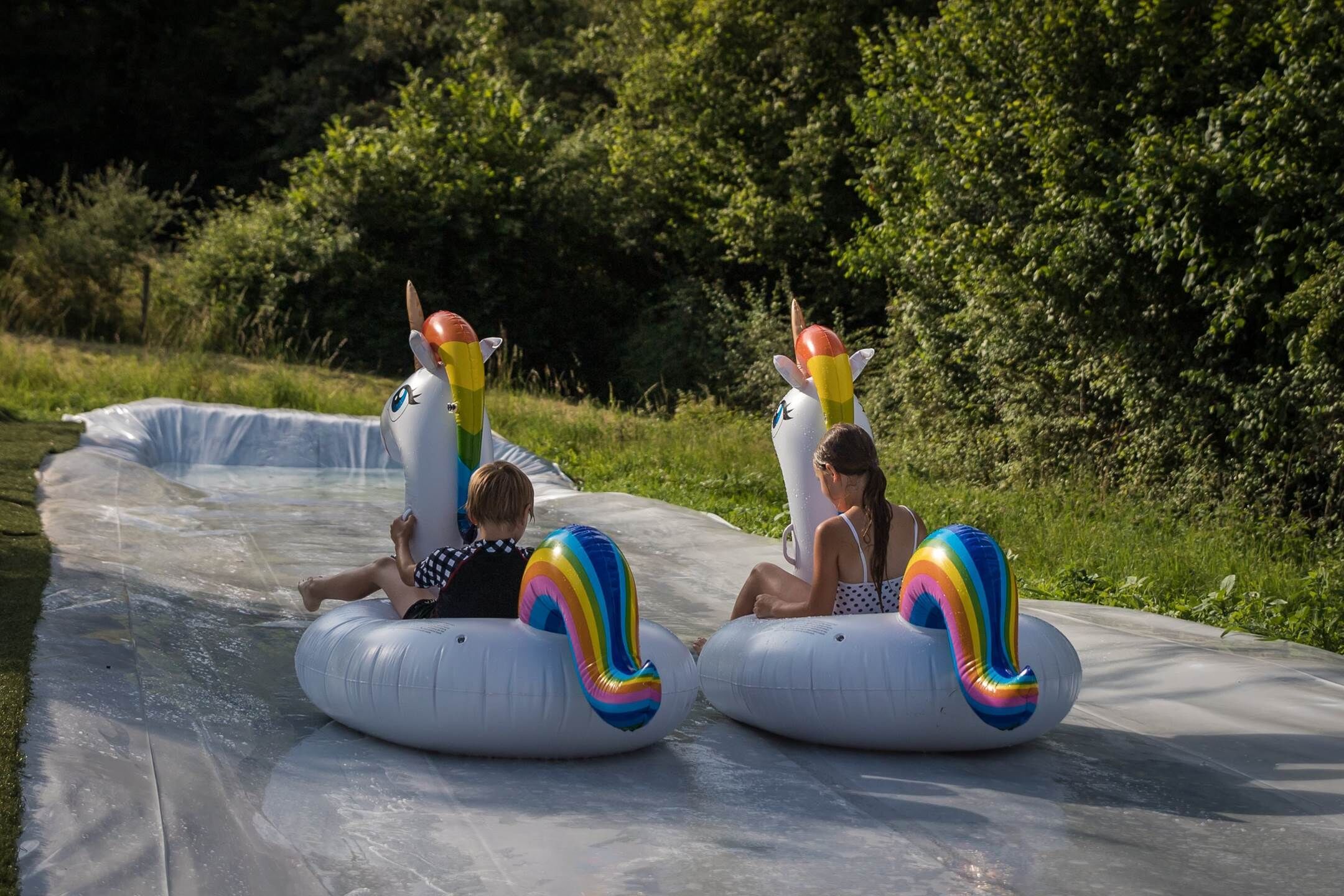Deux personnes, sur des bouées gonflables décorées de motifs de licornes, dévalent une toboggan aquatique.