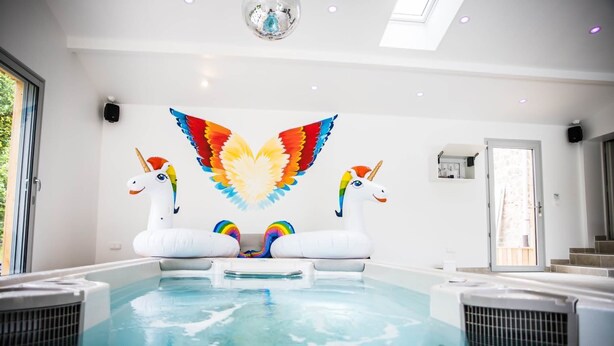En swimmingpool med to svaneformede luftmadrasser, en loftlampe og en dør, der fører til en balkon.