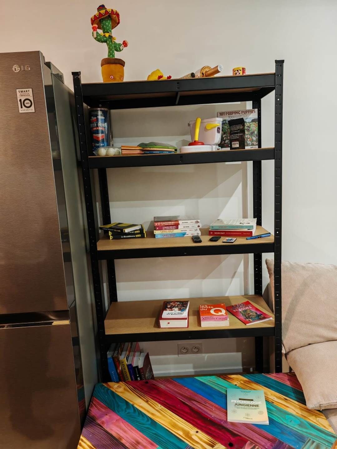 A compact kitchenette with a built-in refrigerator, a shelf with books and a small cactus decoration, and a colorful bedspread.