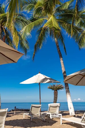 A beach with palm trees, white umbrellas, and lounge chairs. - Luxury 1-bedroom apartment at Icon Vallarta 2-801 with an ocean view (Puerto Vallarta)