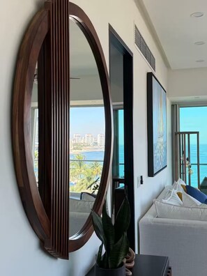 A modern living room with a large mirror, a potted plant, and a view of the ocean and buildings. - Luxury 1-bedroom apartment at Icon Vallarta 2-801 with an ocean view (Puerto Vallarta)