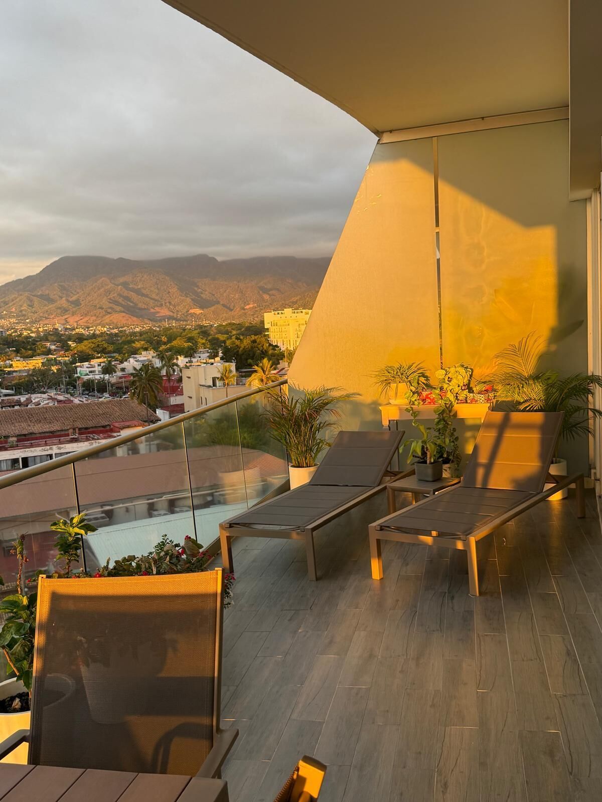 Un balcon agrémenté de chaises longues, de plantes en pot et offrant une vue sur le paysage urbain et les montagnes.