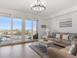 Ein geräumiges Wohnzimmer mit einem großen Schiebeglasfenster zum Balkon, einer beigefarbenen Sofagarnitur, einem weißen Couchtisch und einer Deckenleuchte.